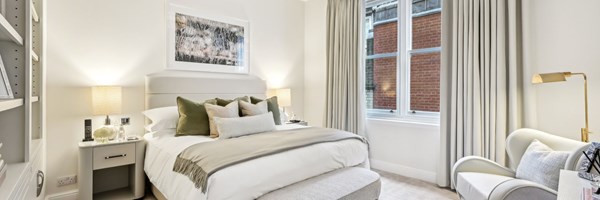 Serene bedroom with neutral palette, layered pillows, soft lighting, and a view of classic brick architecture outside the window.