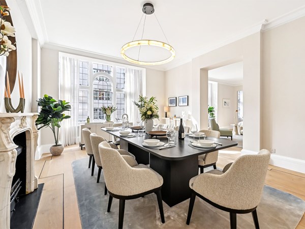 Bright dining room with a dark rectangular table, upholstered chairs, and a large circular chandelier, featuring tall arched windows and floral arrangements.
