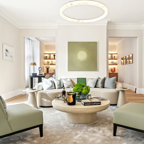 Inviting lounge scene with circular chandelier, curved sofa, neutral palette, and coffee table featuring design books and greenery.
