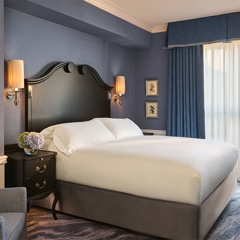 Bedroom view with a dark wood headboard, white bed linens, and matching blue curtains, blending traditional detailing with a calm, refined palette.