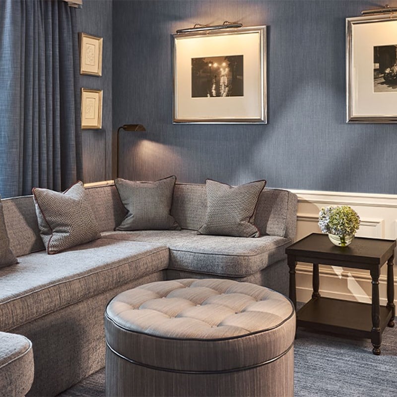 Comfortable living space with a grey L-shaped sofa, framed monochrome prints and a small black side table topped with a vase of flowers.