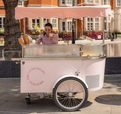 Pink ice-cream cart with a vendor scooping ice cream into a cone on a sunny day.