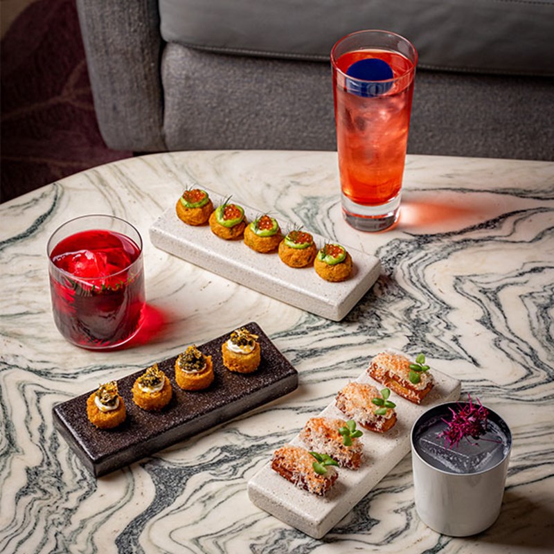 A selection of light bites and vibrant cocktails placed on a marble table.