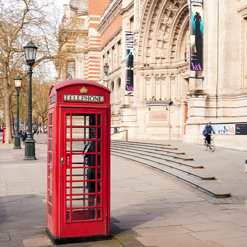 Exterior and entrance of Victoria & Albert Museum with a red phone box outside and old lam posts in the background.