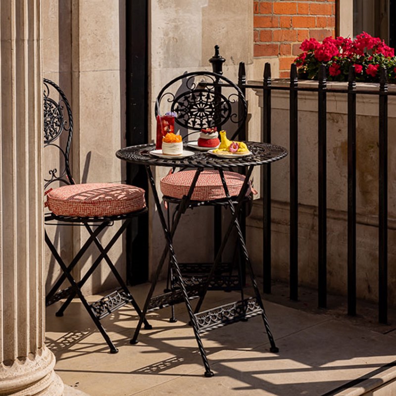 Two chairs and a table outside The Connaught Patisserie on the terrace, with a selection of cakes and a refreshing drink placed on the table.